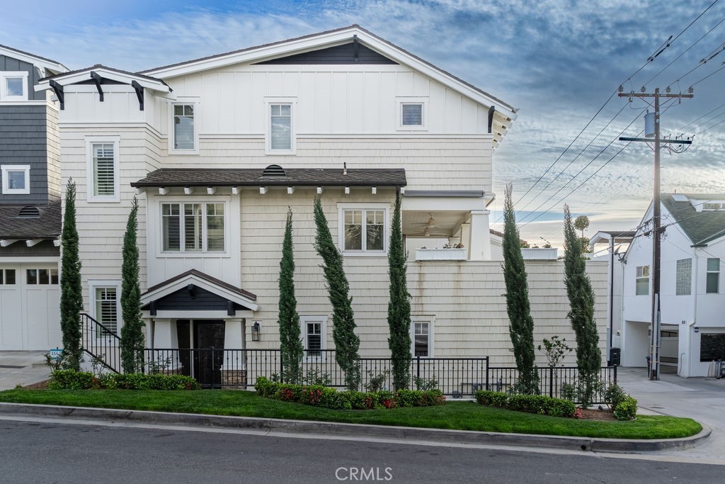 White multi-story house with shingle siding, cypress trees, and a landscaped front lawn.