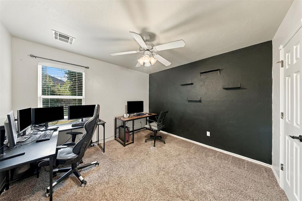 Home office with computer desks and monitors, a window with blinds, and a dark accent wall.