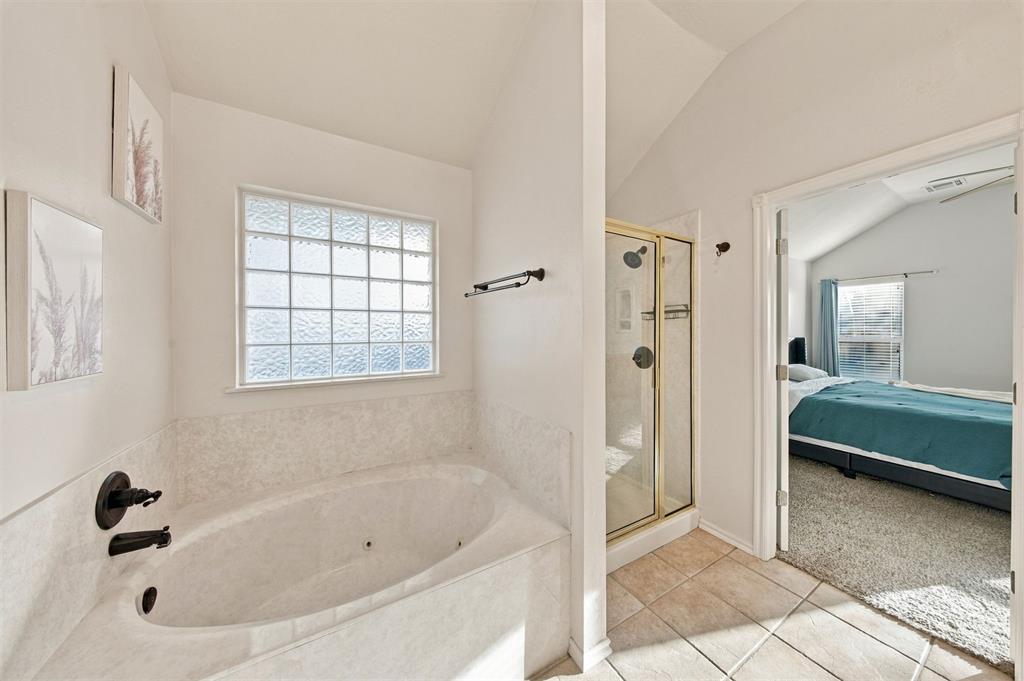 Primary bathroom with a corner soaking tub, glass-block window, and adjoining bedroom with a teal bedspread.