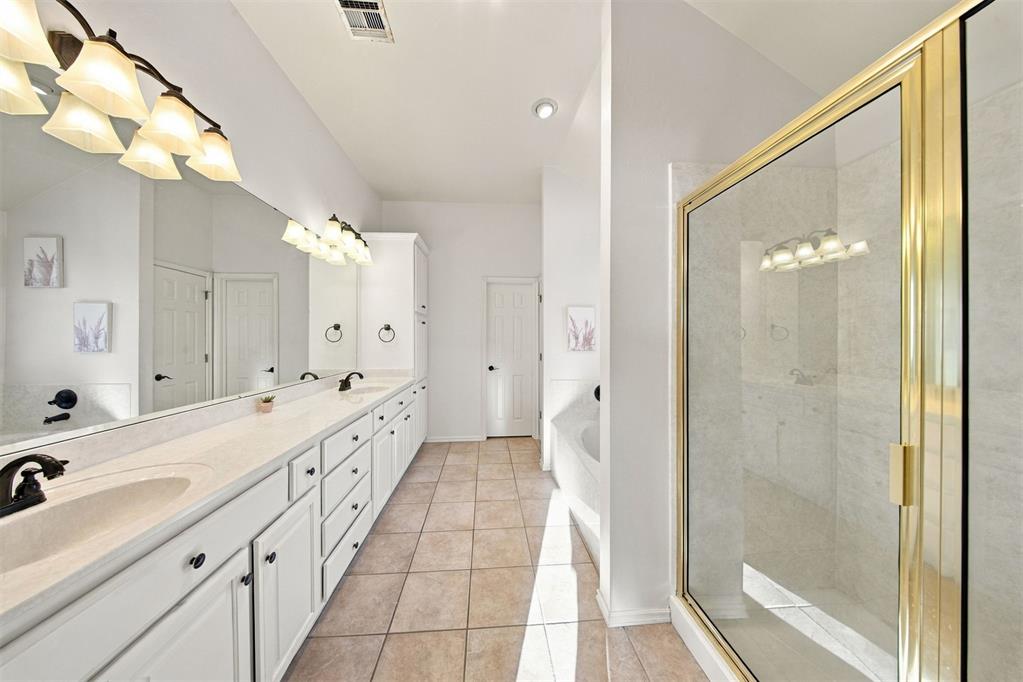 Primary bathroom with a long double vanity and glass shower with gold-tone trim.