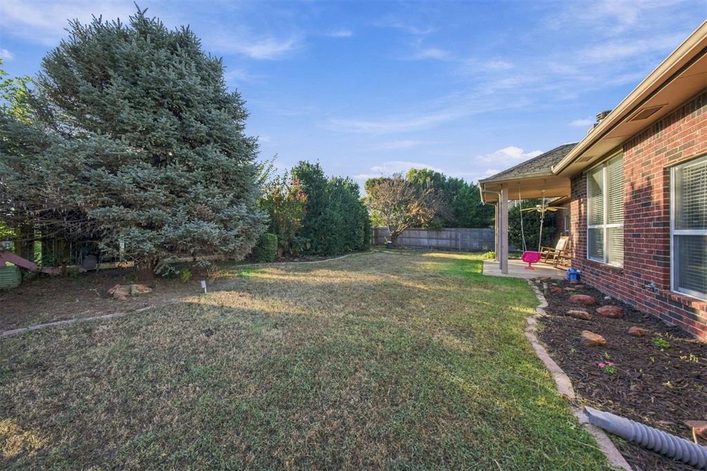 Backyard with a broad lawn, mature evergreen tree, and covered patio with a swing.