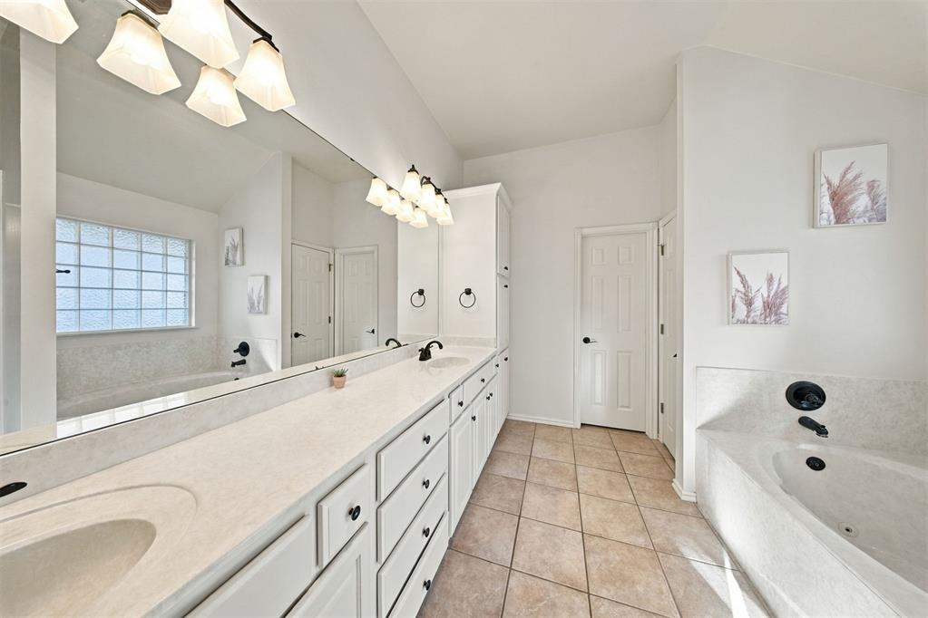 Bathroom with a long white vanity, wall-length mirror, and built-in soaking tub.