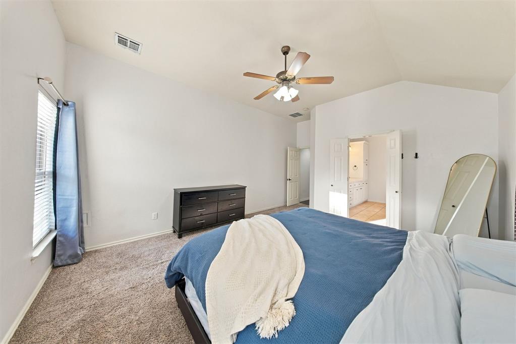 Bedroom with a blue-covered bed, black dresser, and open doorway to a tiled bathroom.