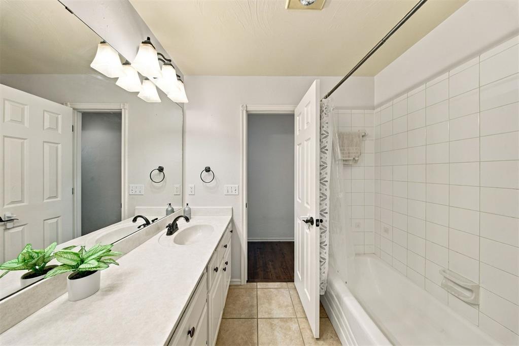 Bathroom with a double-sink vanity, large mirror, and white tiled bathtub and shower.