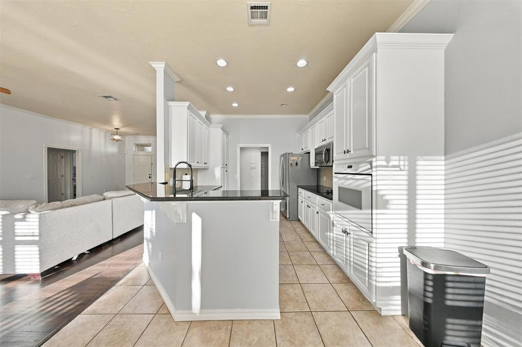 Open-plan kitchen with a large dark-countertop island, white cabinetry, stainless steel appliances, and adjoining living area.
