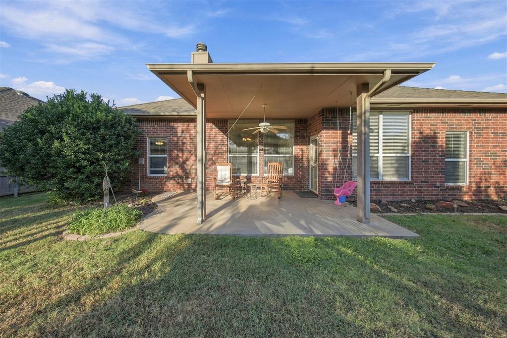 Covered patio with outdoor seating and ceiling fan at the rear of a brick home.