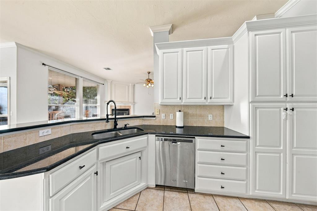 Kitchen with white cabinets, black countertops, stainless dishwasher, and a window above the sink.