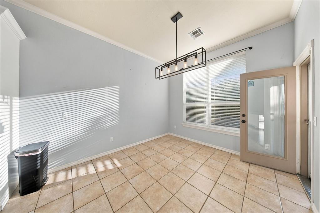 Empty dining room with tan tile floors, a hanging chandelier, large windows, and a glass-panel door.