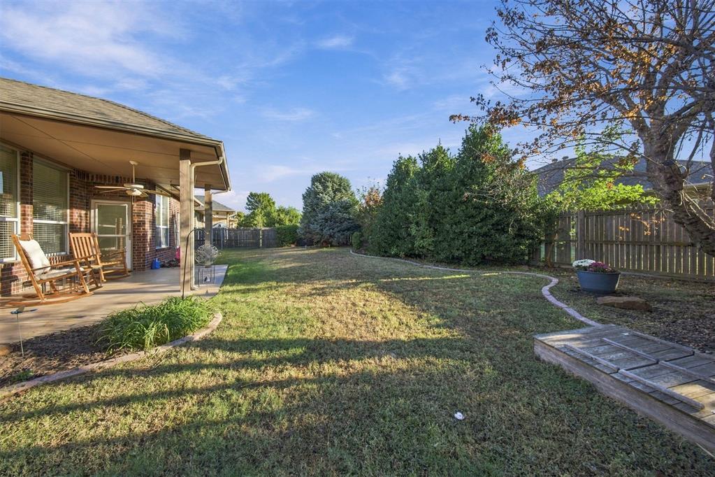 Fenced backyard with a lawn, curved garden border, and covered patio with rocking chairs.