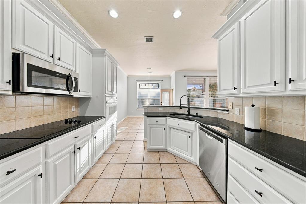 Kitchen with white cabinets, black countertops, stainless steel appliances, and beige tile flooring.