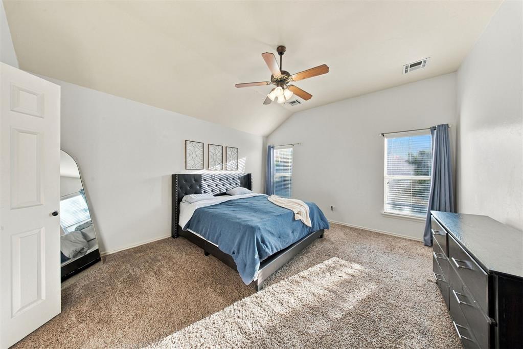 Bedroom with blue bedding, a black tufted headboard, beige carpet, and two windows.