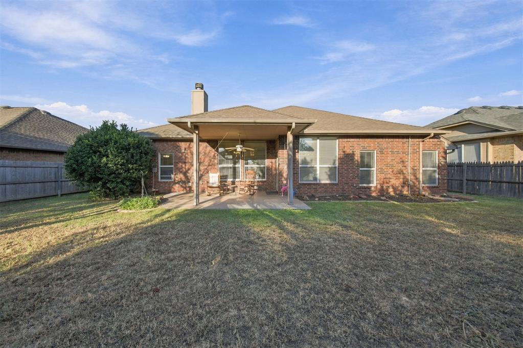 Rear brick exterior with covered patio, outdoor seating, fenced yard, and broad lawn.