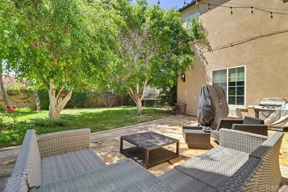 Backyard patio with woven seating, a green lawn, and mature shade trees.
