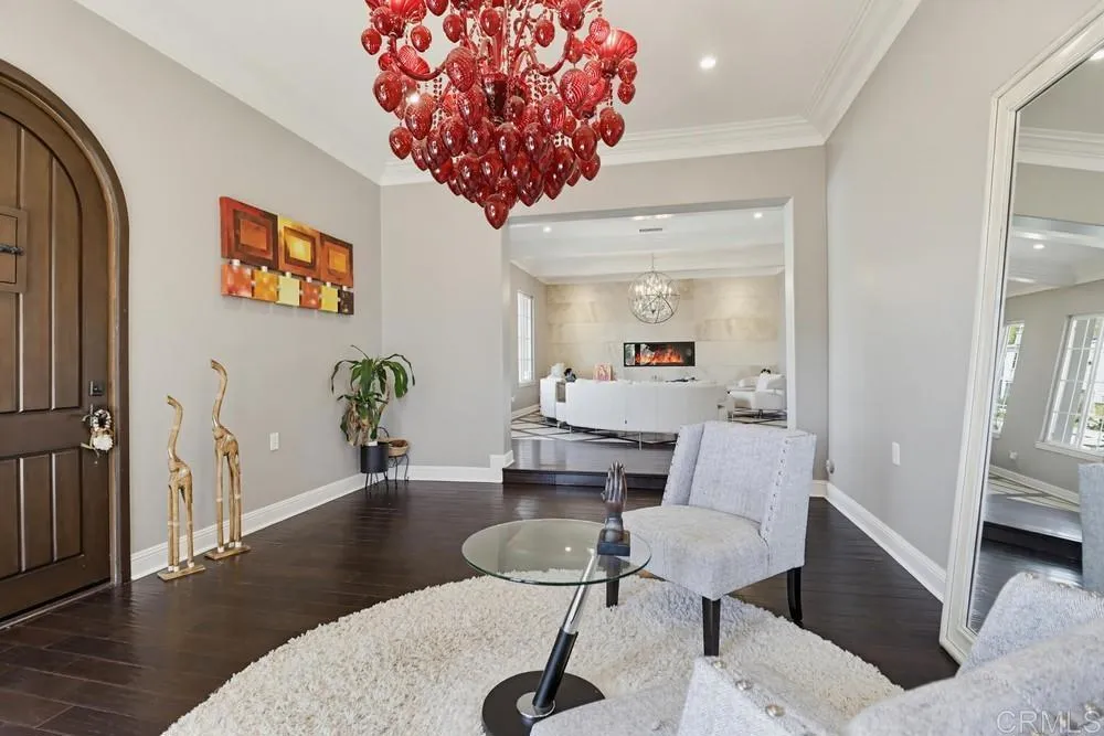 Furnished entry hall with a red glass chandelier, arched front door, and view into a living room with fireplace.