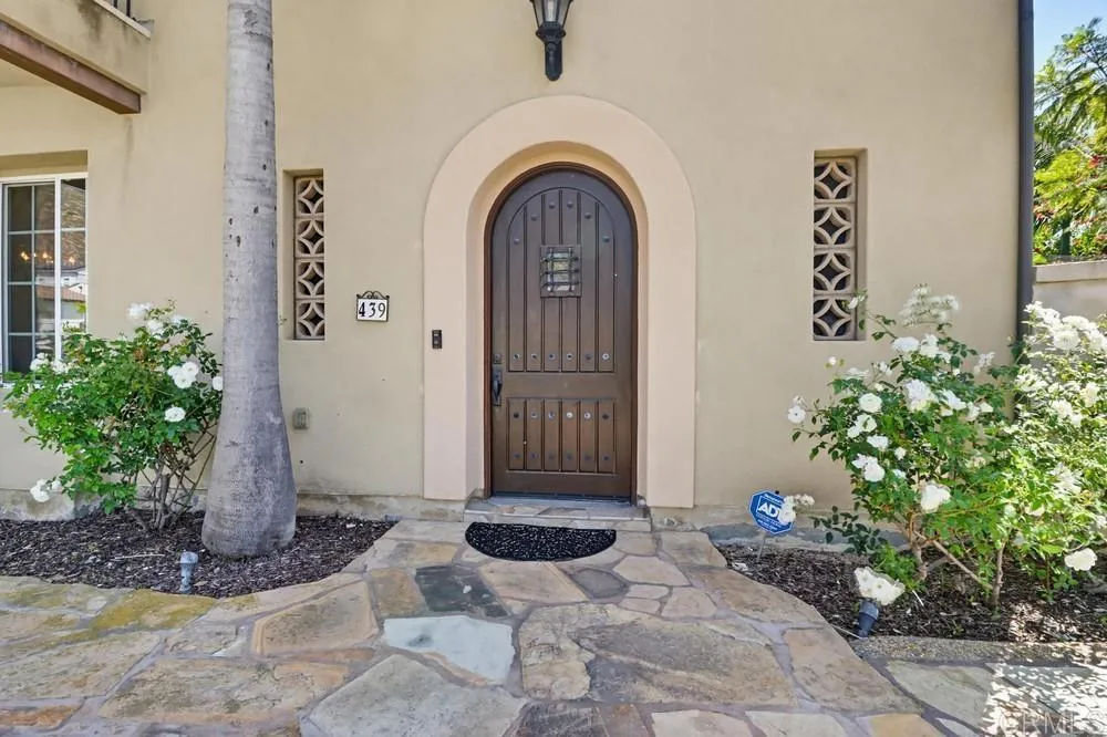 Home entrance with an arched wooden door, stone walkway, and white flowering shrubs.