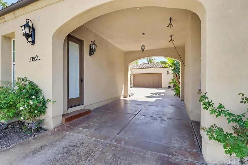 Covered arched driveway leading toward a garage, with stucco walls and decorative lanterns.