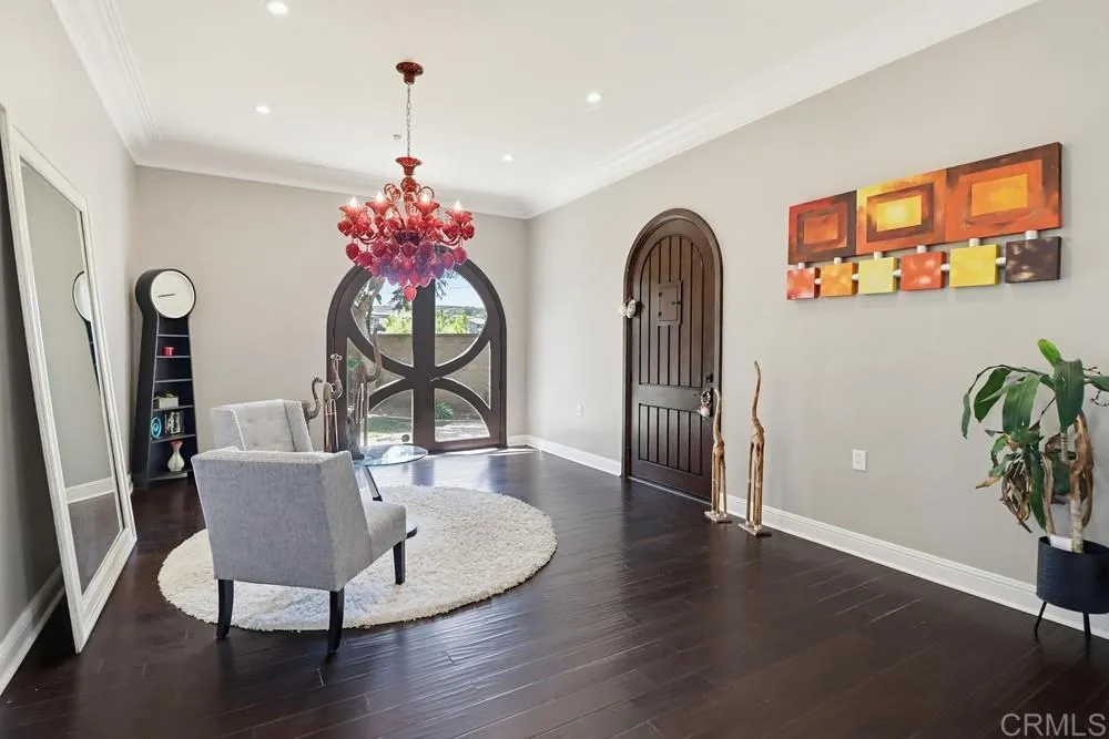 Furnished entryway with dark floors, a red chandelier, and a distinctive arched glass front door.