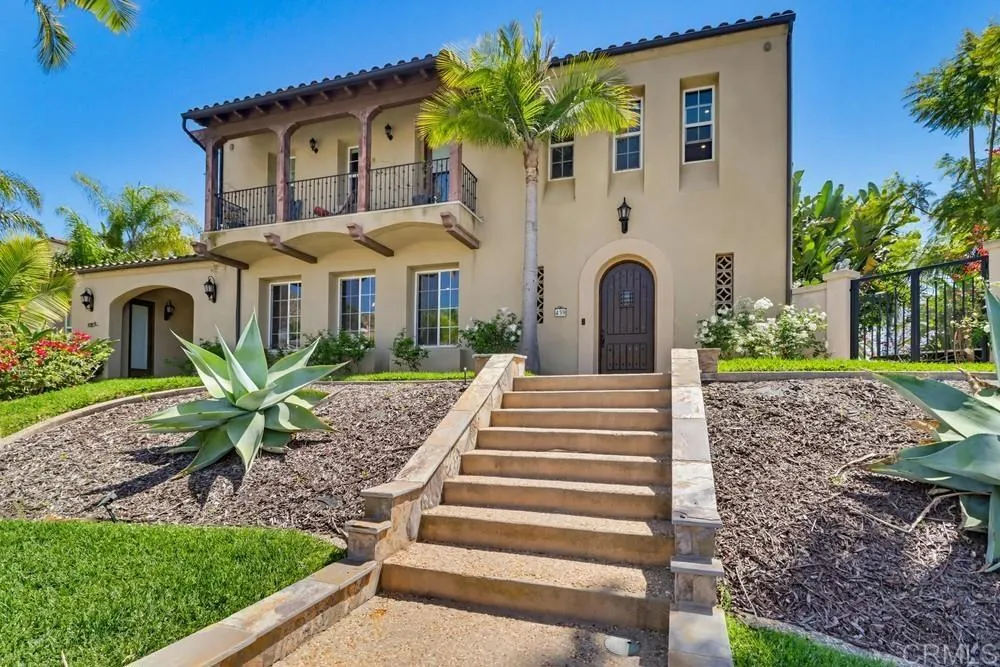 Two-story stucco home with a balcony, broad front steps, palm trees, and agave landscaping.