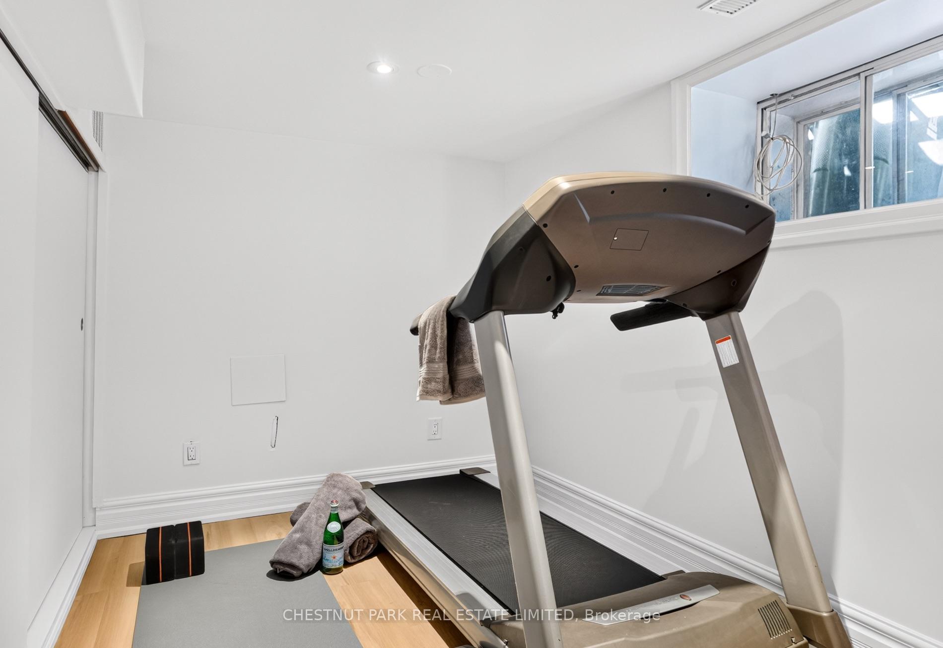 Home gym with a large treadmill, exercise mat, and weights beside a high window.