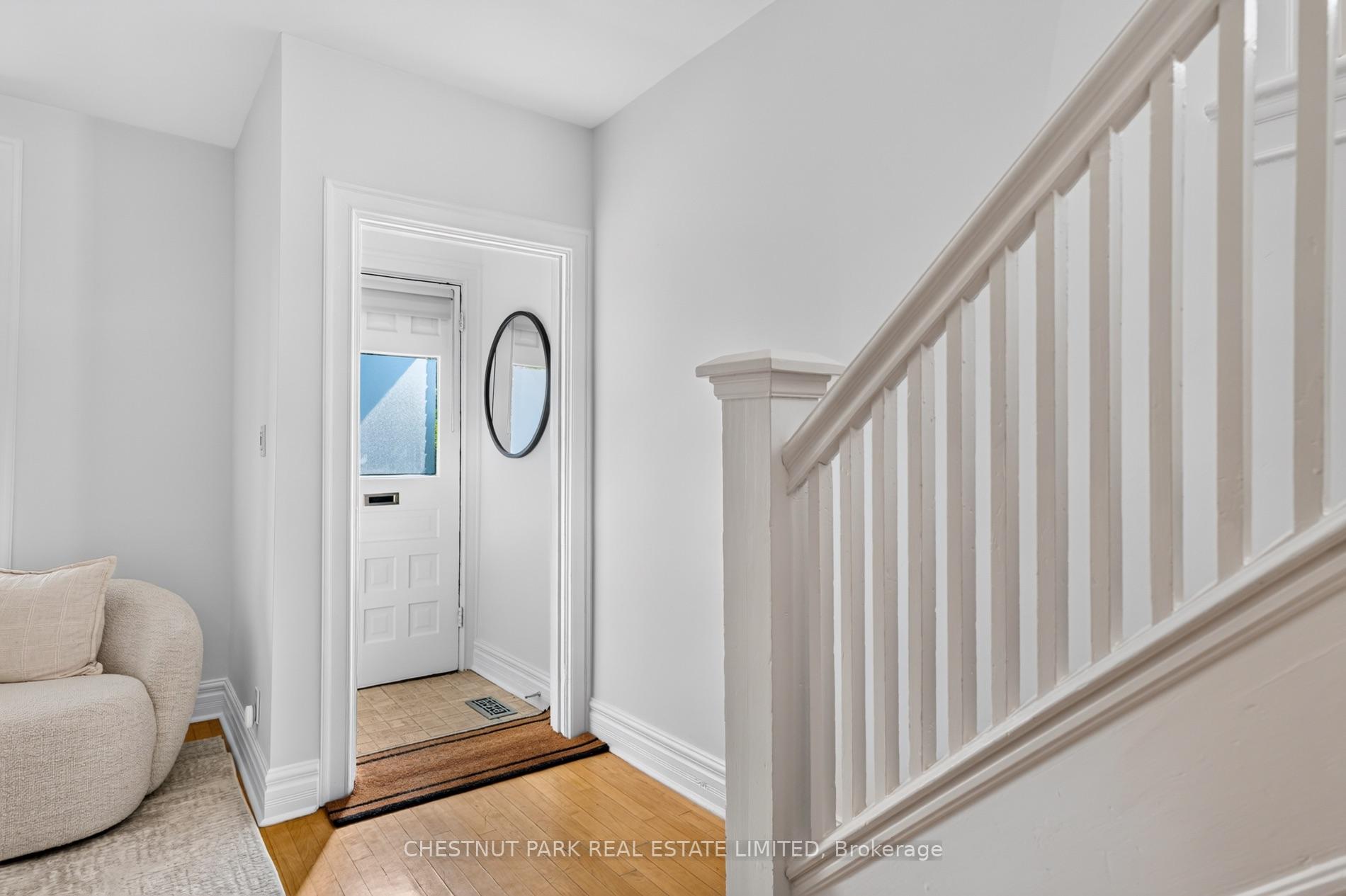 Entry hall with a white front door, oval mirror, hardwood floor, and white staircase railing.