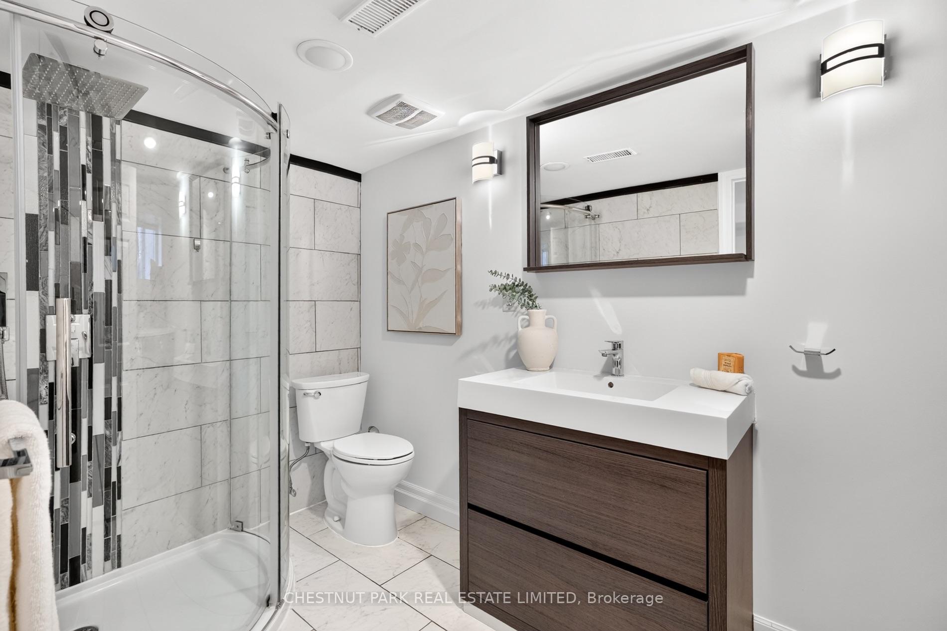 Modern bathroom with a curved glass shower, marble-look tile, and dark wood vanity.