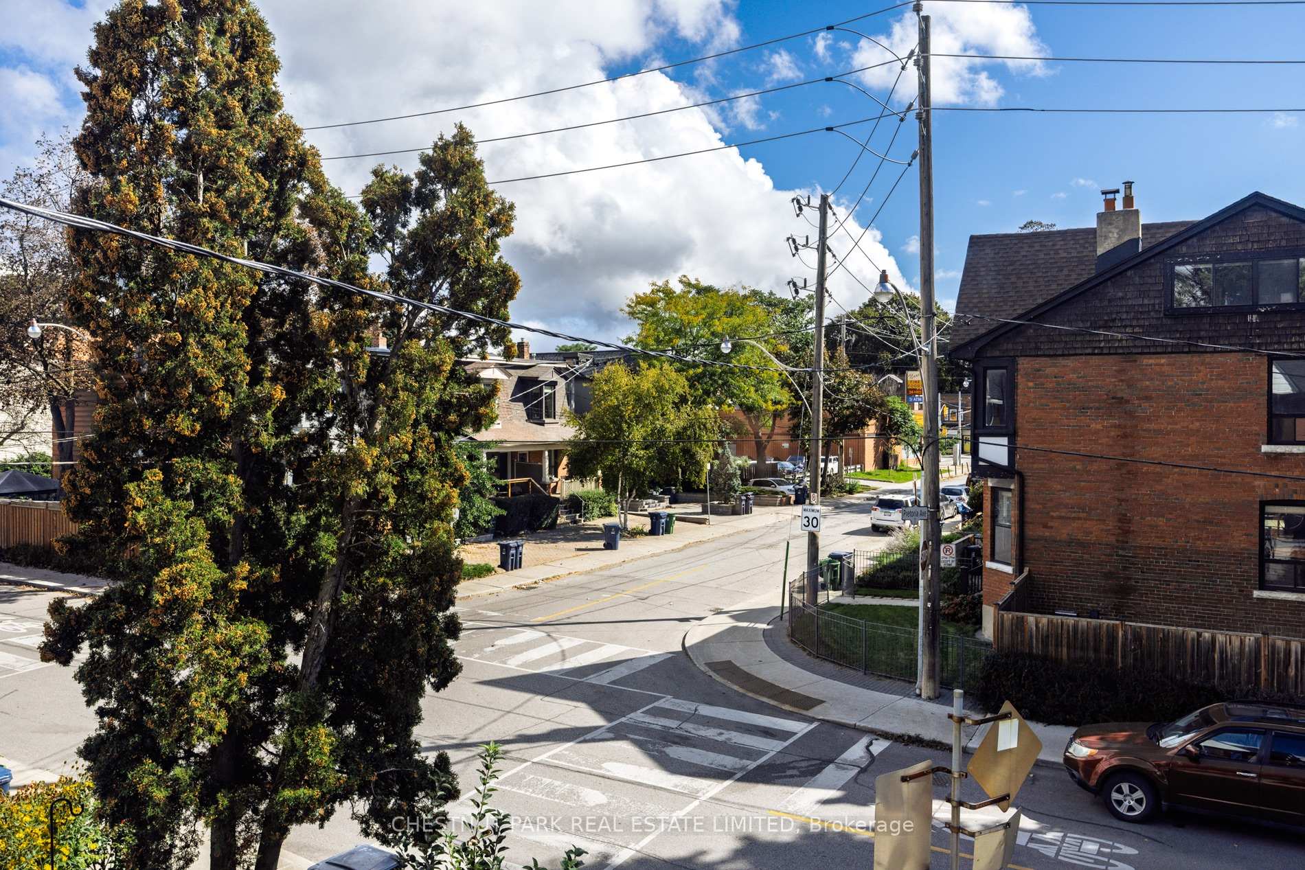 Residential street intersection with detached homes, mature trees, and overhead utility lines.