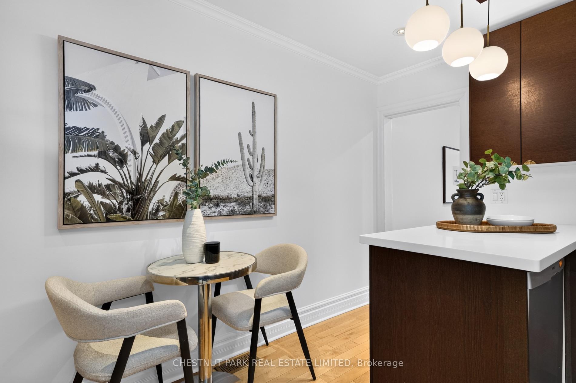 Dining area beside a kitchen island, with upholstered chairs, botanical prints, and globe pendant lights.