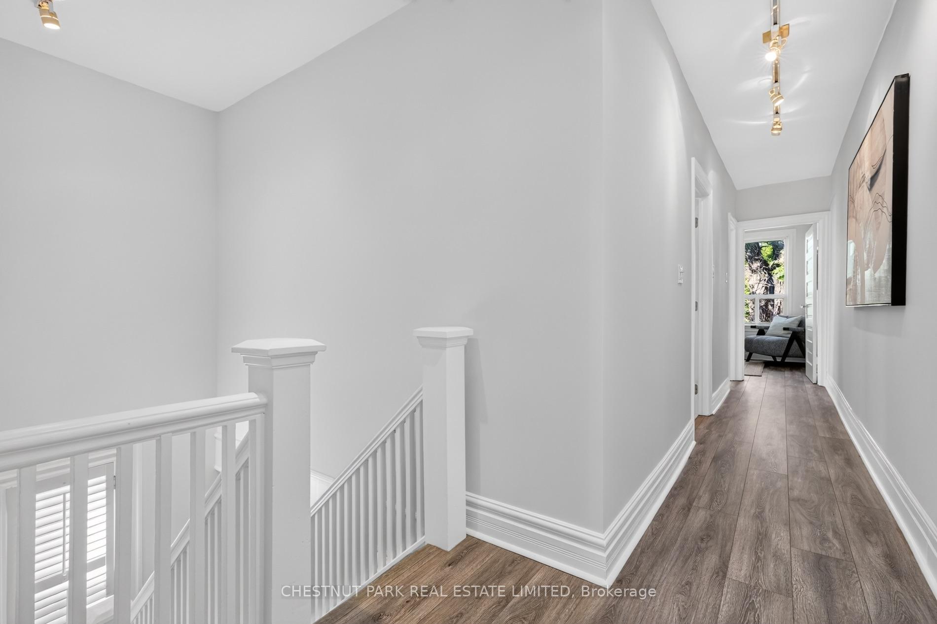 Hallway with dark wood-look flooring, white stair railing, and a sitting area visible through the doorway.