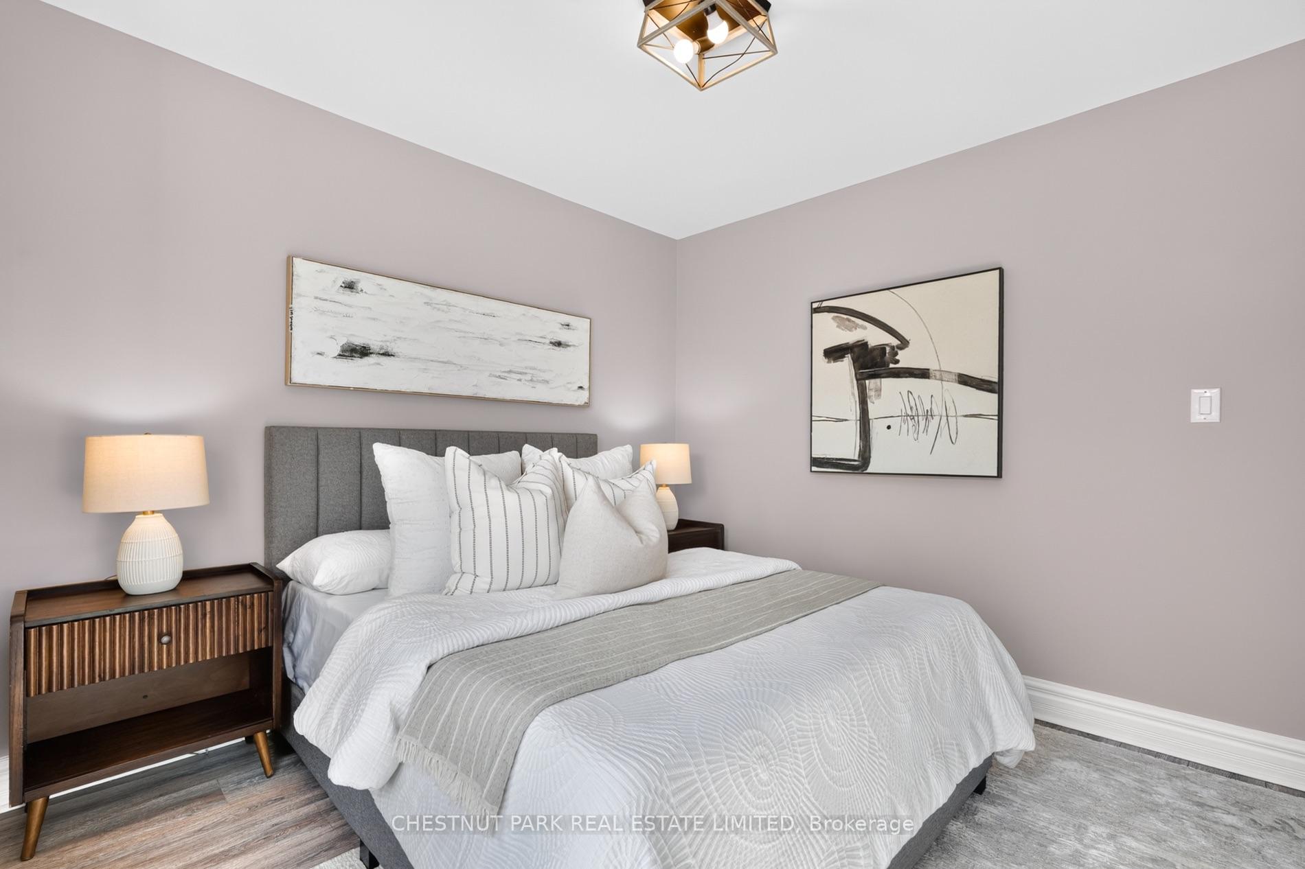 Furnished bedroom with white bedding, a gray throw, mauve walls, and abstract artwork.