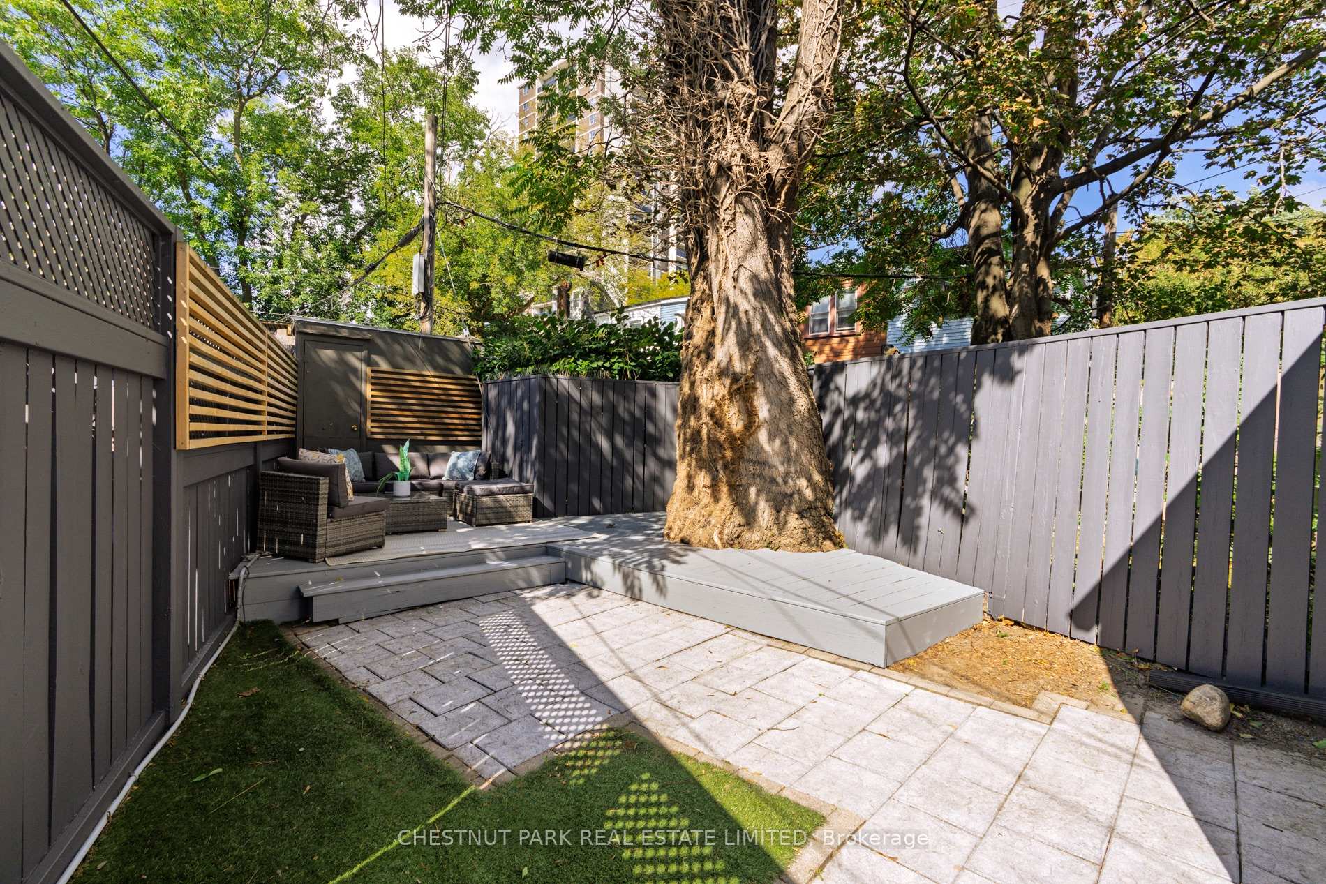 Backyard patio with wicker seating on a raised deck beneath a large mature tree.