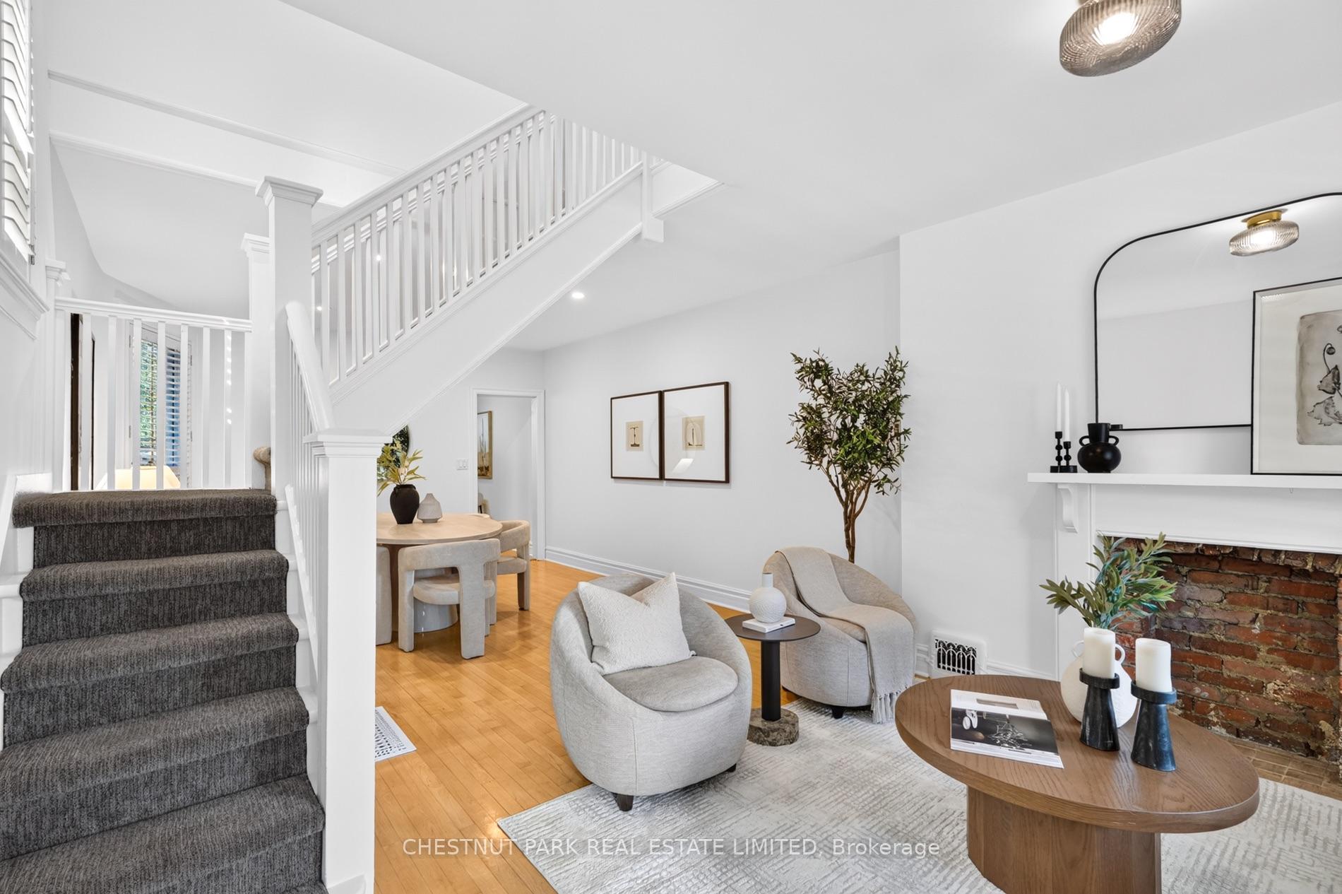 Living room with a carpeted staircase, hardwood floors, dining area, and brick fireplace