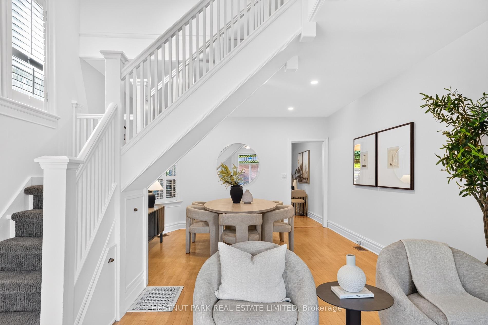 Dining area beneath a white staircase, with a round table, upholstered chairs, and hardwood floors.