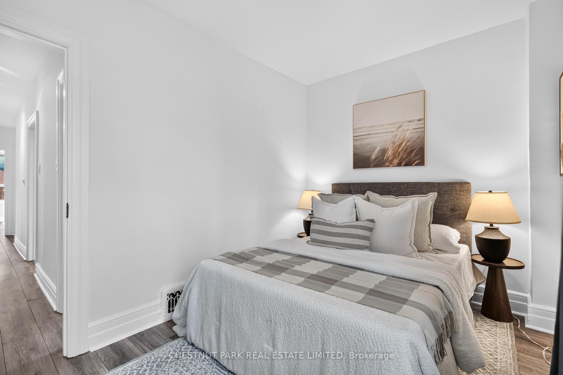 Staged bedroom with layered gray-and-white bedding, dark headboard, bedside lamps, and beach grass artwork.