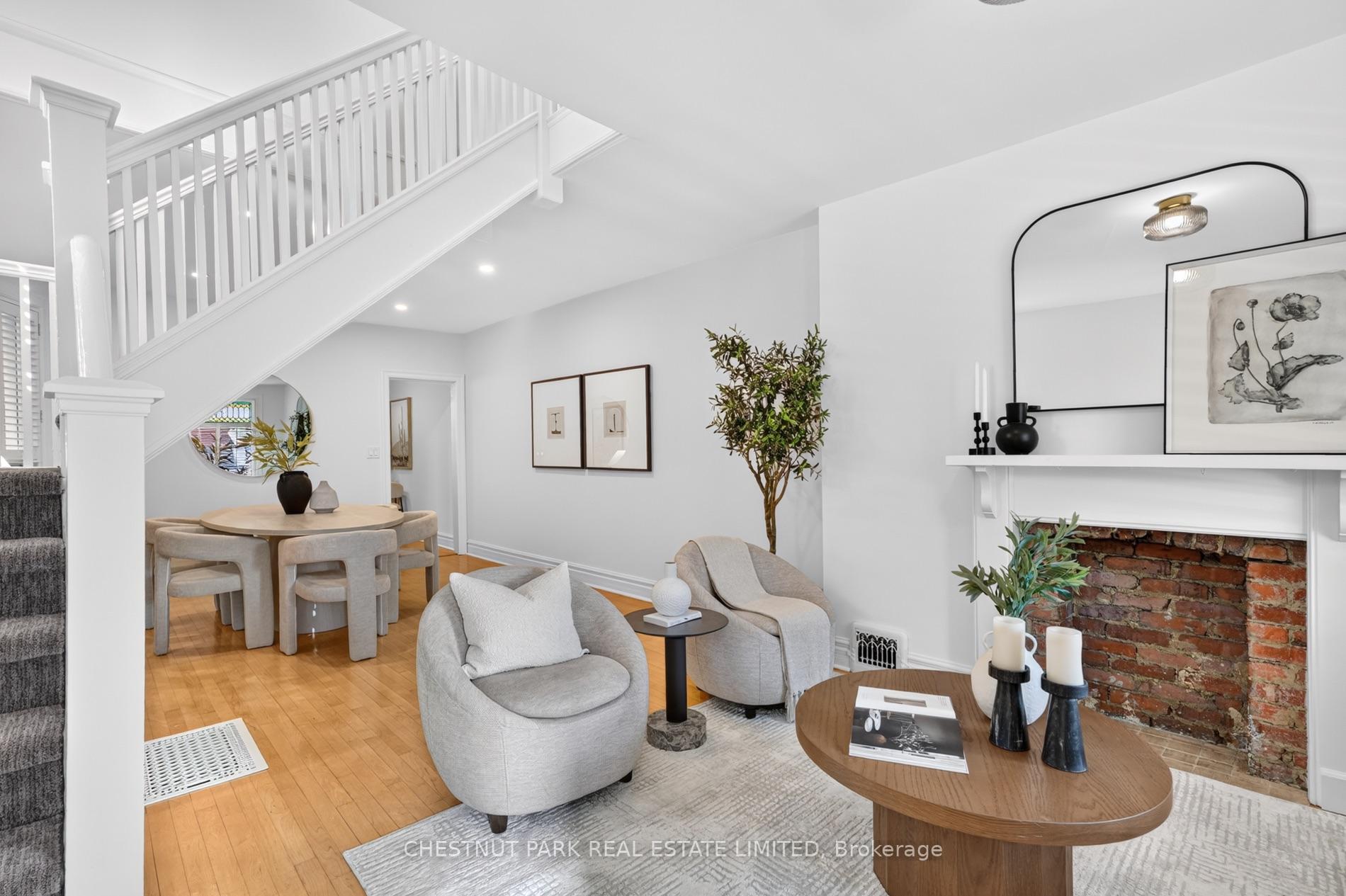 Living room with a brick fireplace, white staircase, and adjoining dining area.