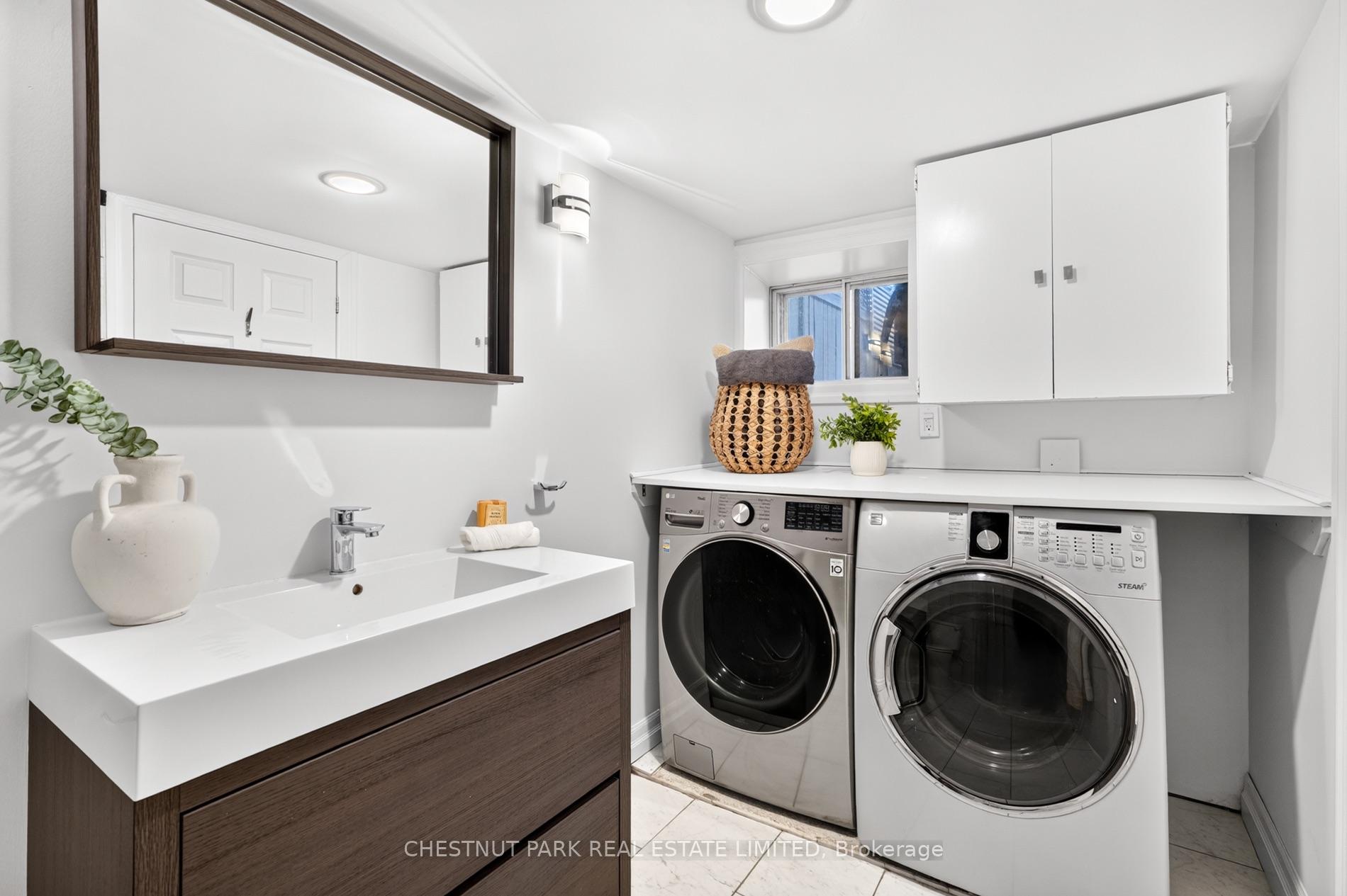 Laundry room with a white sink vanity, front-loading washer and dryer, and overhead cabinets.