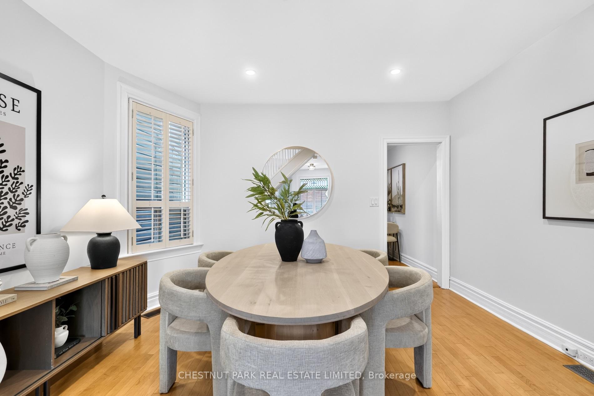 Dining room with a round wood table, upholstered chairs, shuttered window, and circular mirror.