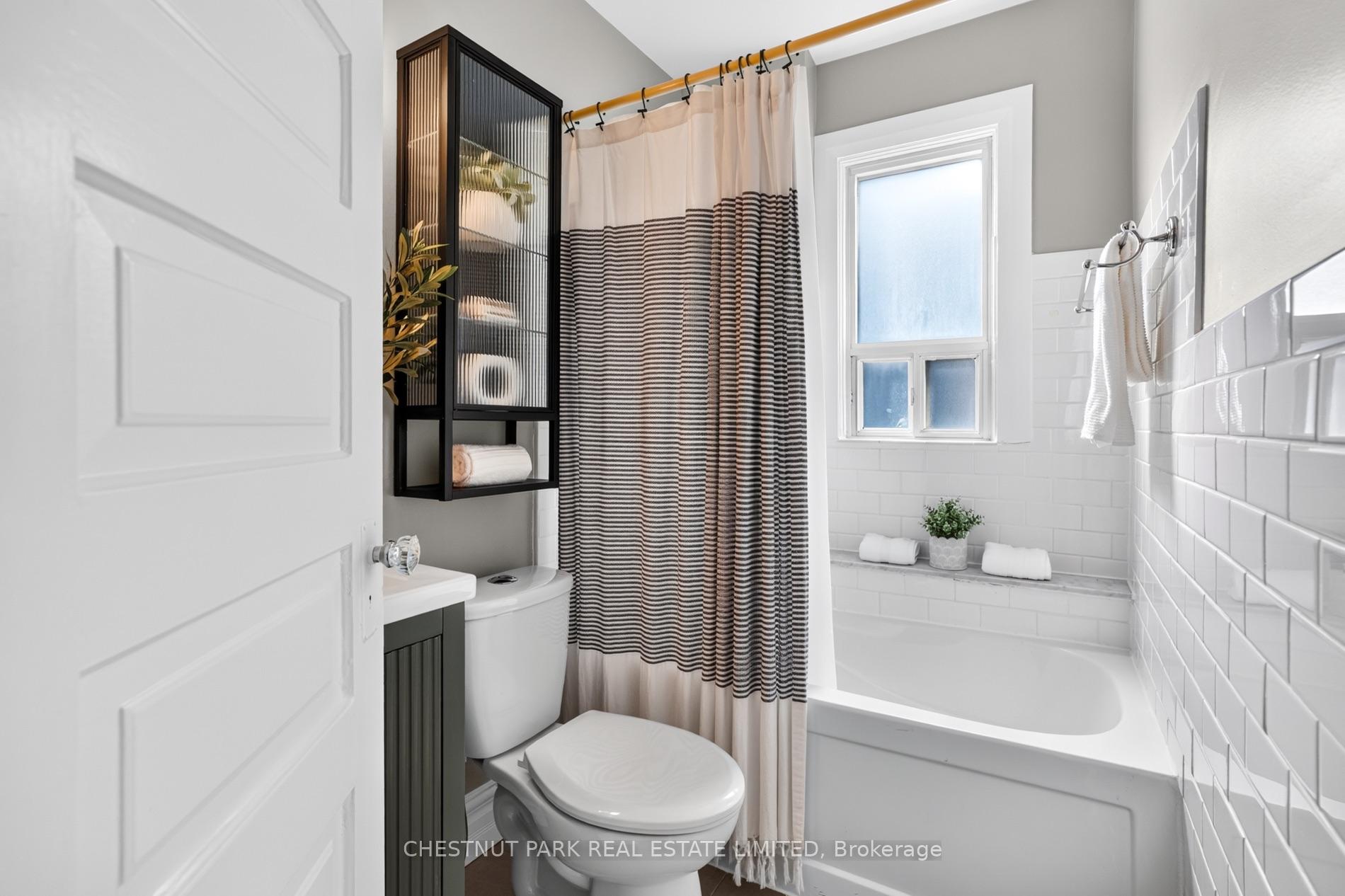 Bathroom with a white tub, subway tile, striped shower curtain, and frosted window.