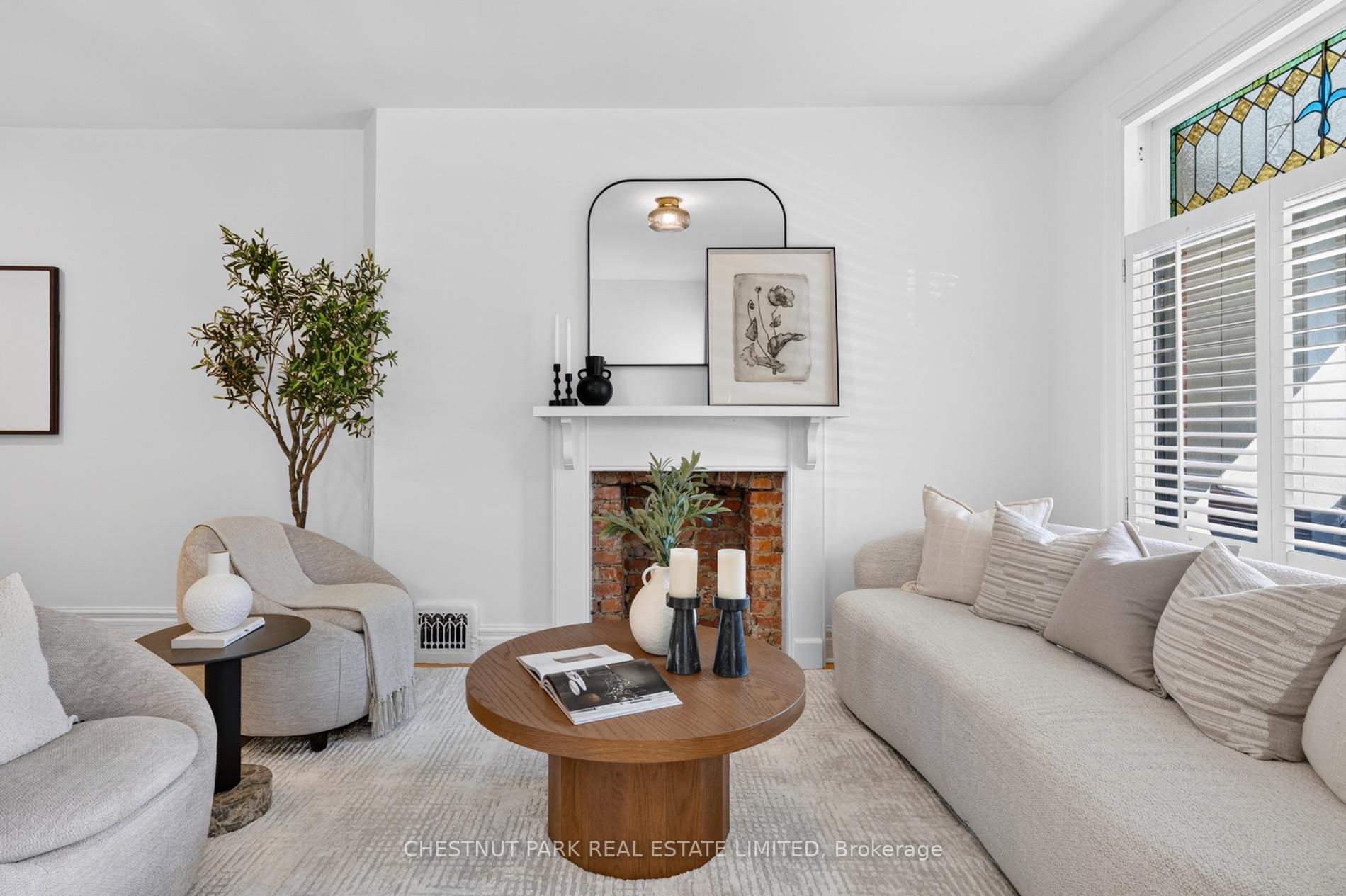 Living room with pale seating, a brick fireplace, and stained-glass transom window.