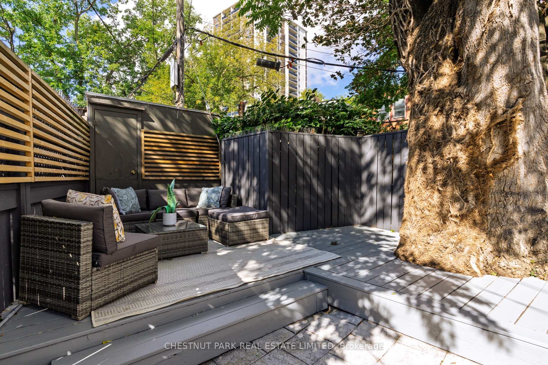 Furnished backyard patio with a gray sectional, wood-slat fencing, and a large mature tree.