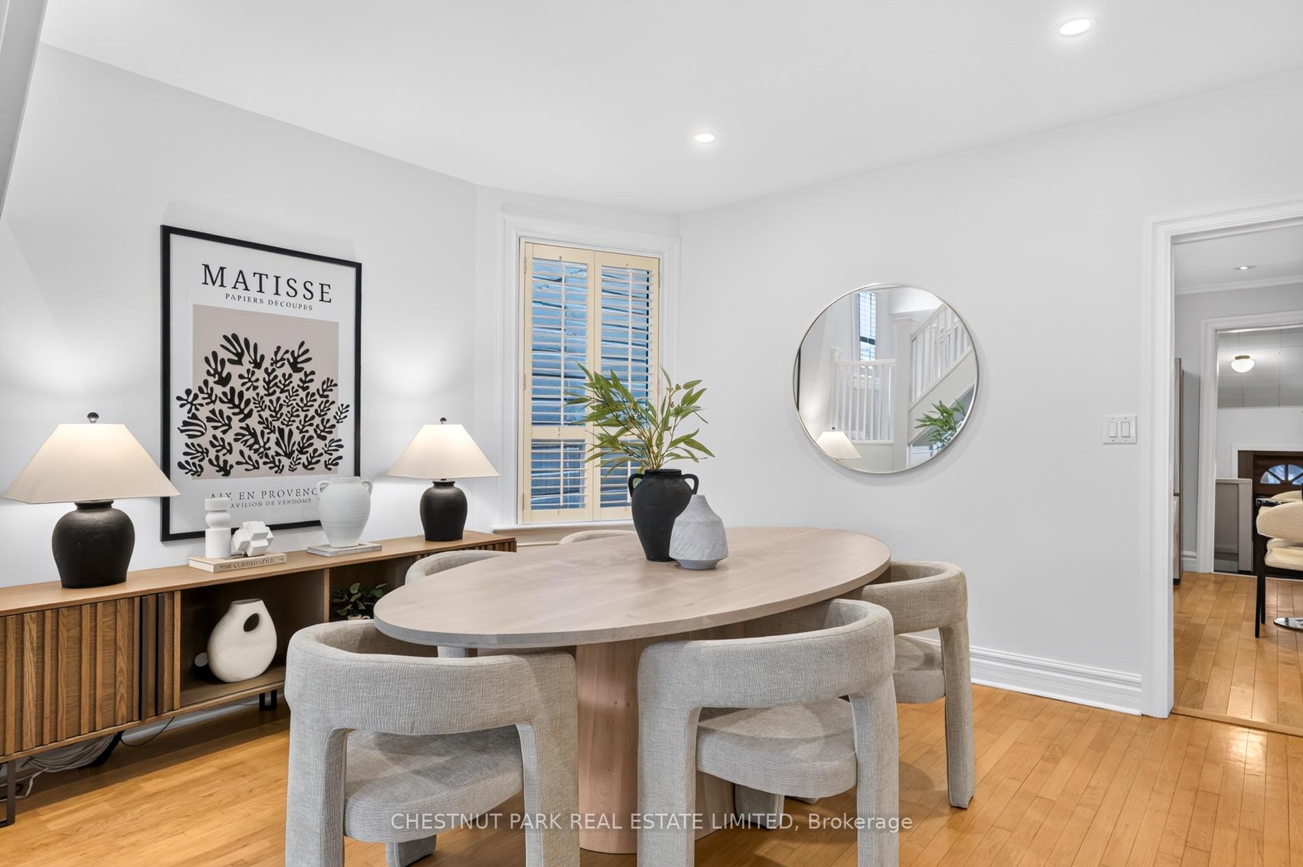Dining room with an oval table, upholstered chairs, wood sideboard, hardwood floors and a shuttered window.