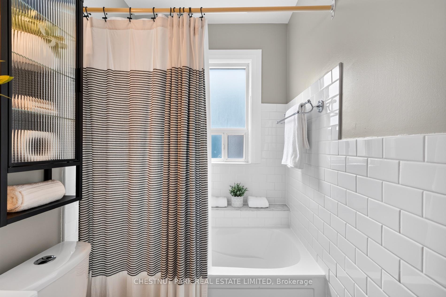 Bathroom with a striped shower curtain, white subway tile, and a frosted window above the bathtub.