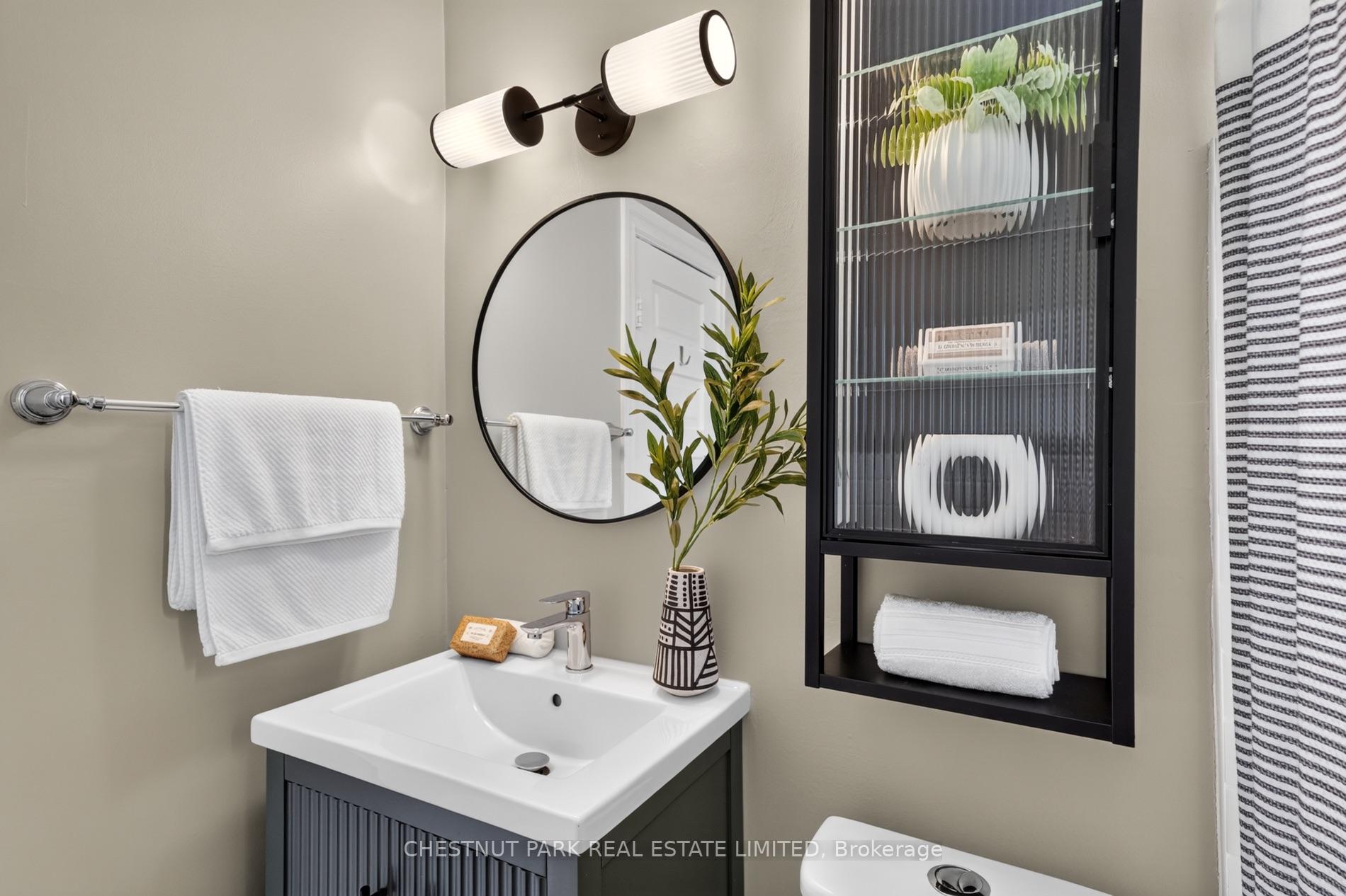 Bathroom vanity with a round mirror, black display cabinet, and white sink.