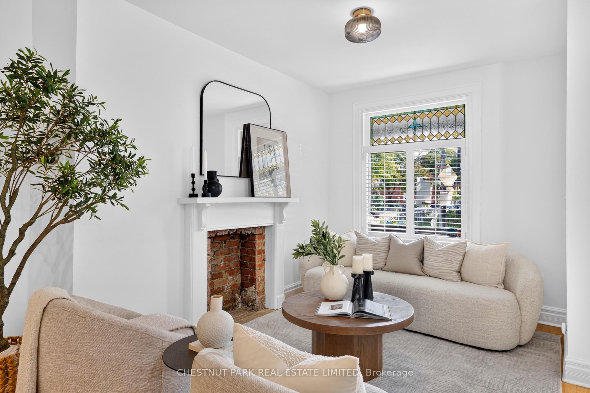 Staged living room with a brick fireplace, pale seating, and a stained-glass window transom.