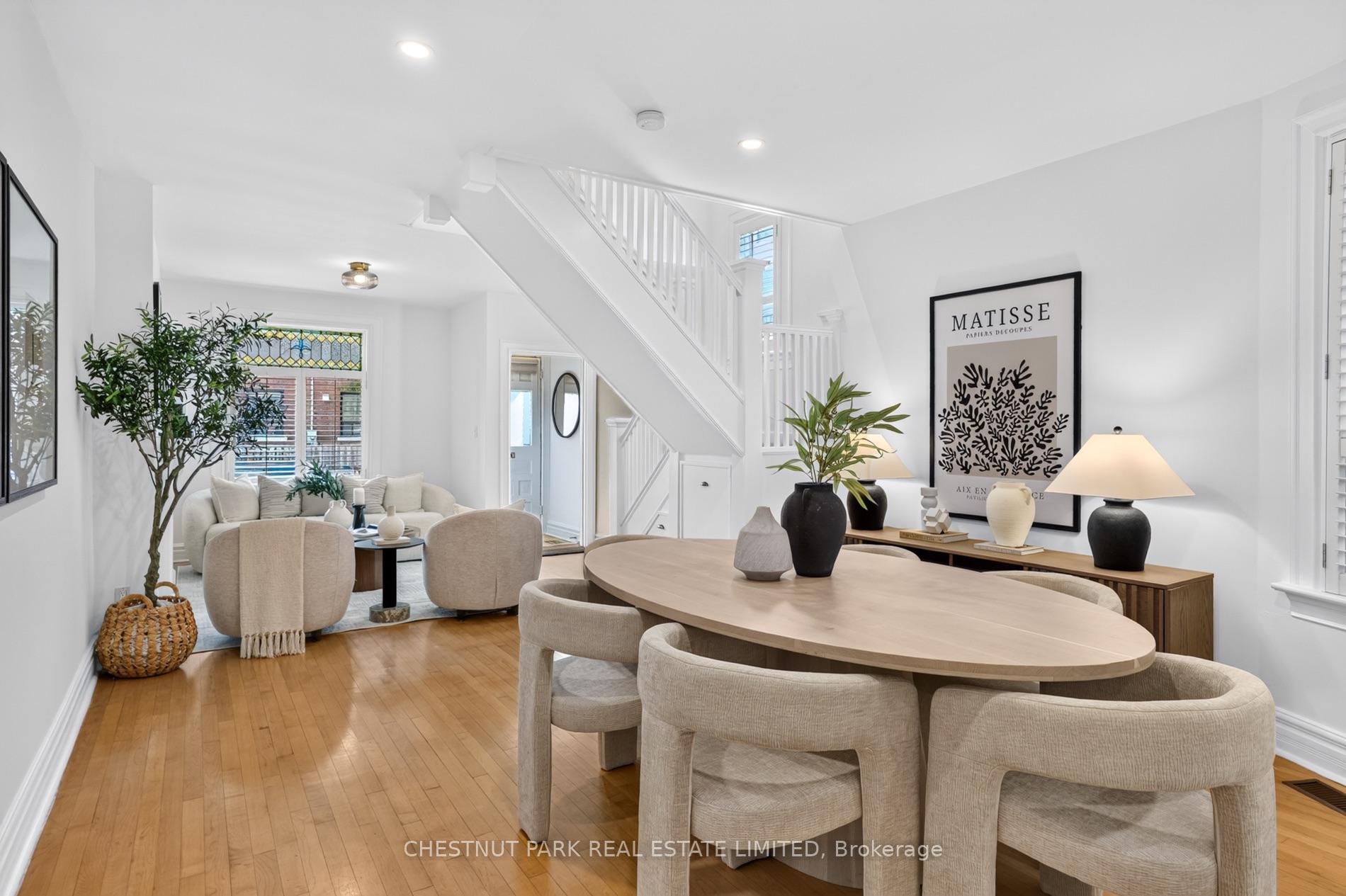 Staged dining and living room with an oval table, hardwood floors, and a white staircase.