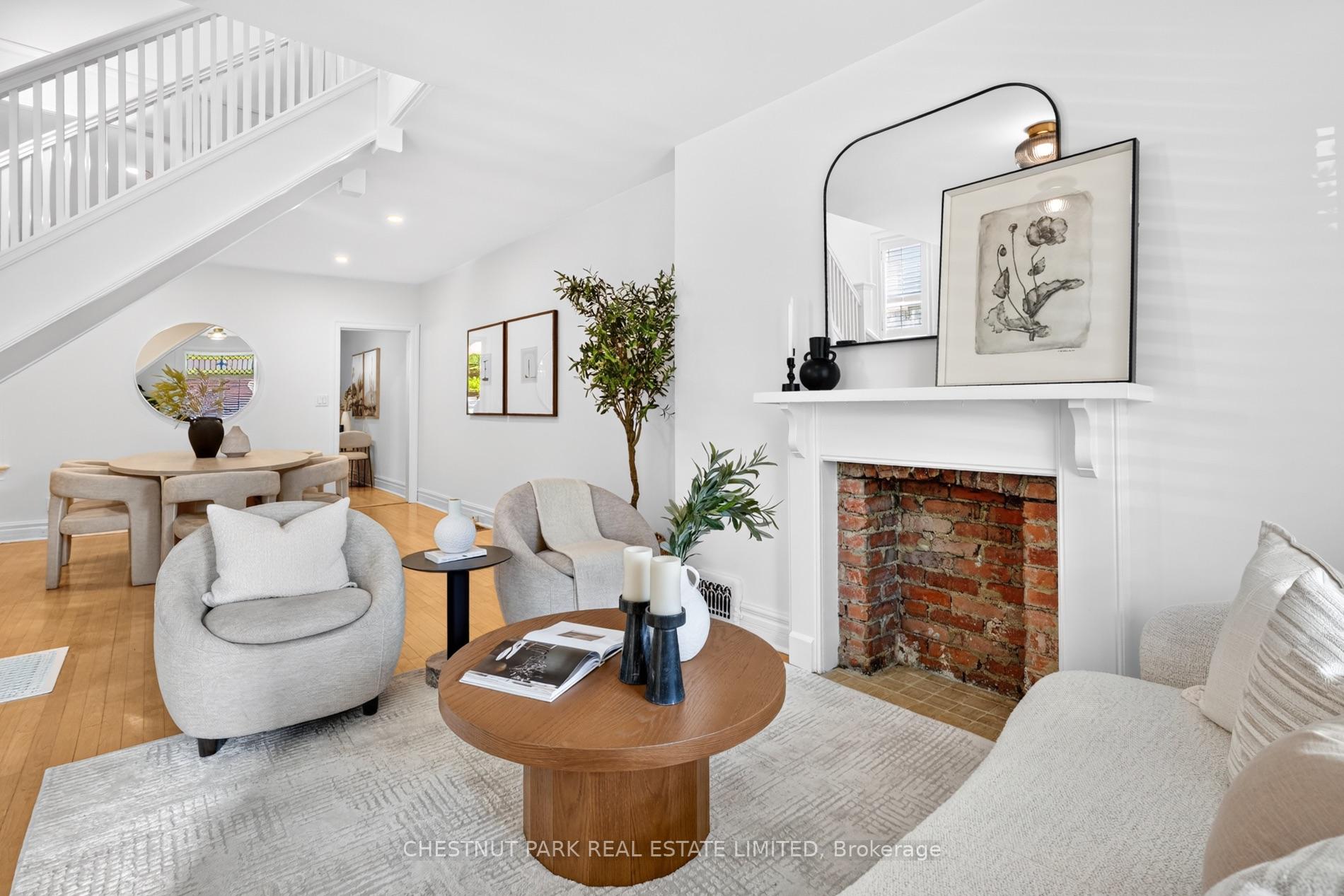 Open-plan living and dining room with a white staircase and exposed-brick fireplace.