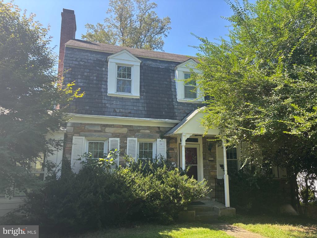 Two-story stone-and-shingle house with dormer windows and a white covered front entry.