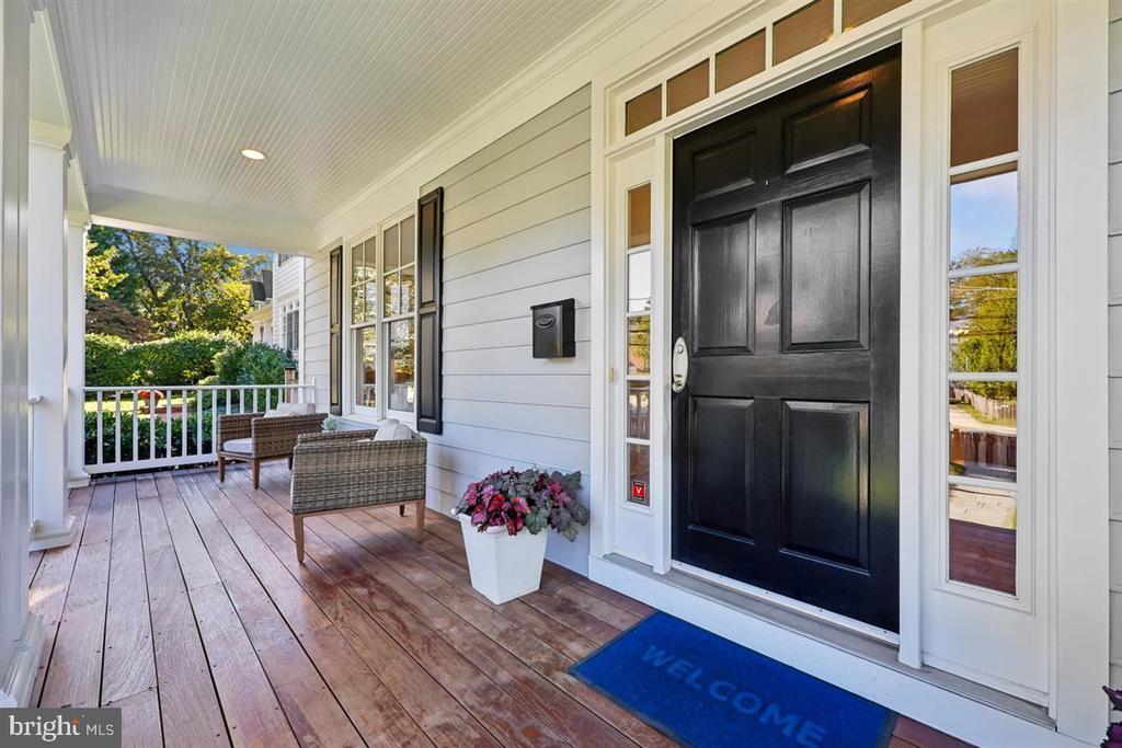 Covered front porch with a black paneled door, wicker chairs, and a potted flower arrangement.