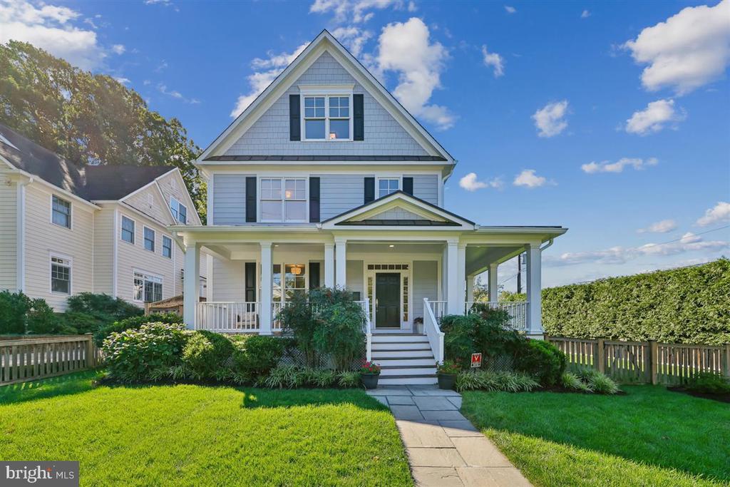 Light blue two-story house with a covered porch, stone walkway, and fenced green lawn.