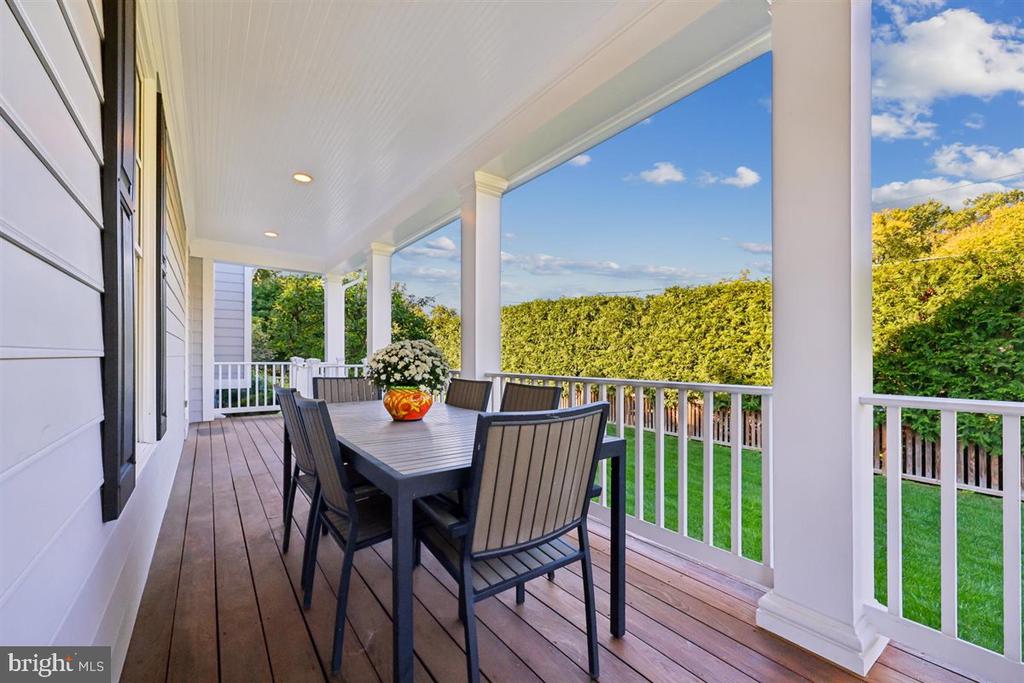 Covered porch with an outdoor dining table overlooking a green lawn and tall hedge.