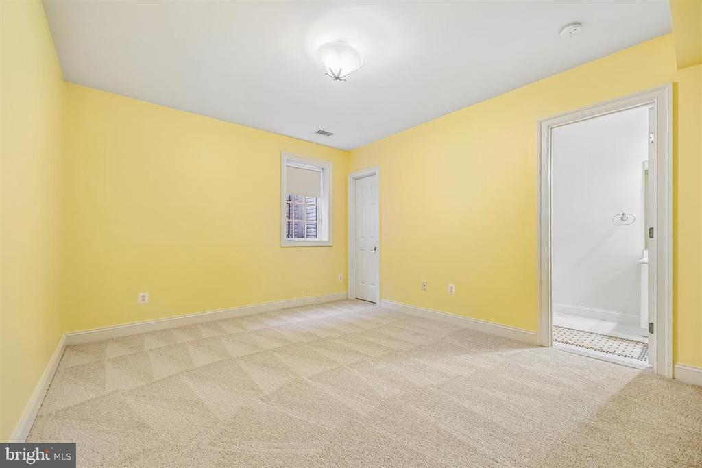 Empty yellow bedroom with beige carpet and an open doorway to the bathroom.